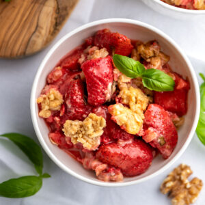A bowl of strawberry crisp with basil leaves and walnuts.