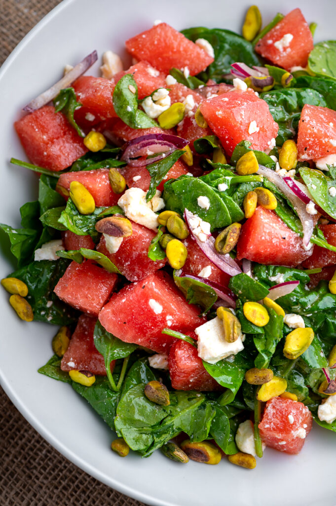 Watermelon salad with feta and spinach in a white bowl.