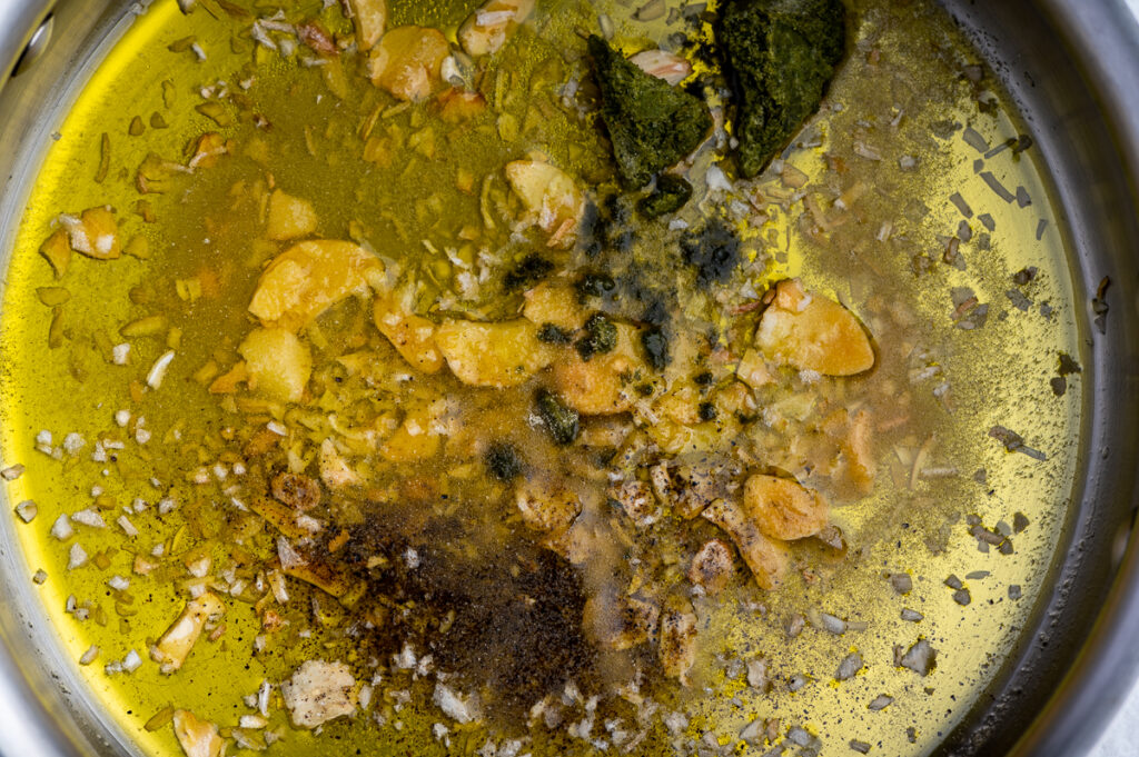 Spices being tossed in olive oil in a skillet.