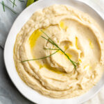 A white bowl filled with creamy cauliflower mash with a garnish of chives.