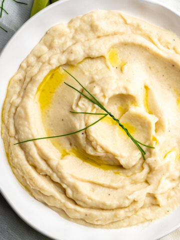A white bowl filled with creamy cauliflower mash with a garnish of chives.