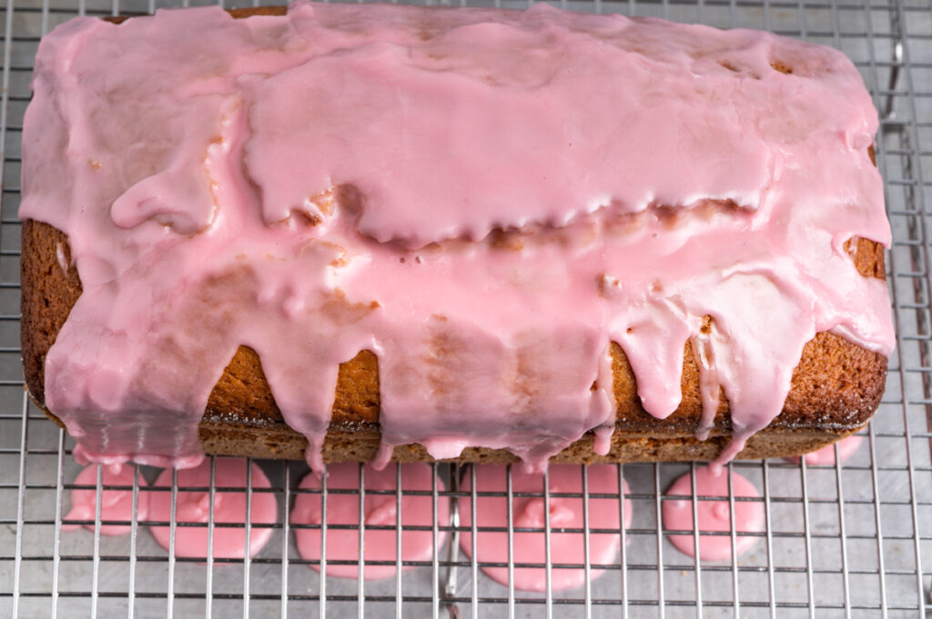 Pink icing over a blood orange olive oil loaf pooling on a baking sheet.