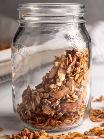 A jar of salted cinnamon nut granola with pieces scattered in front of it.