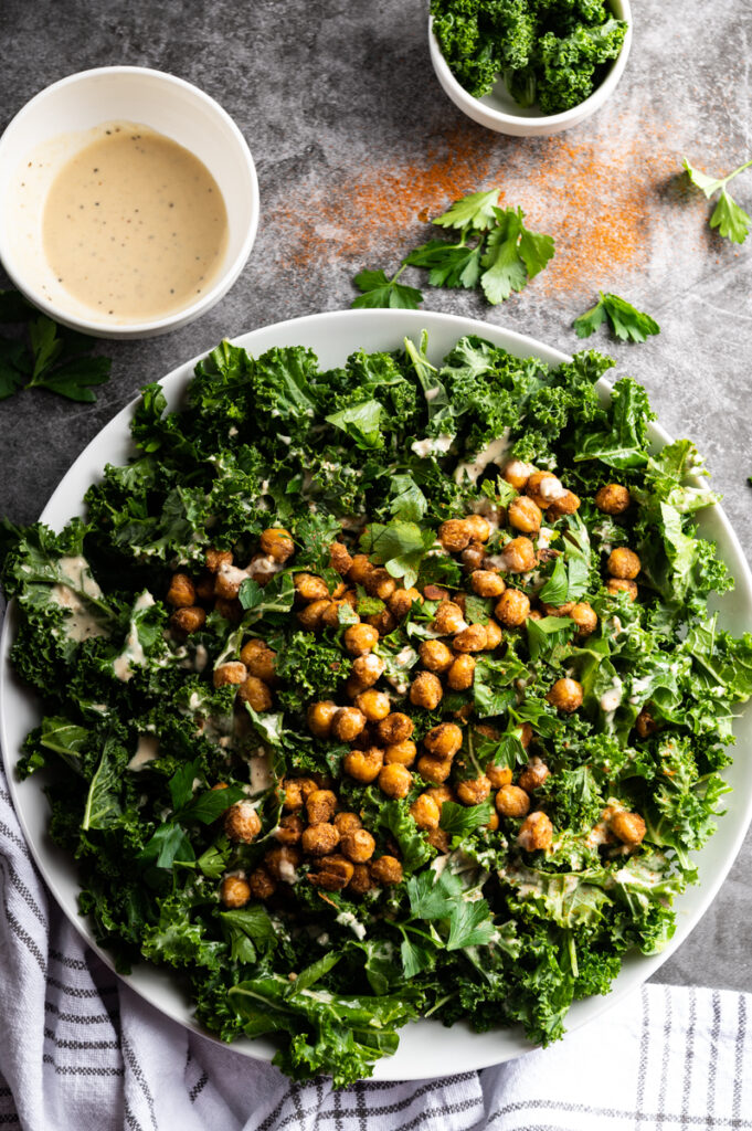 A white platter with kale and chickpeas with a small bowl of tahini dressing.