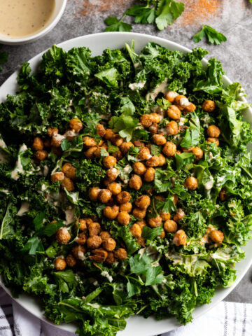 A white platter with kale and chickpeas tossed with tahini dressing.