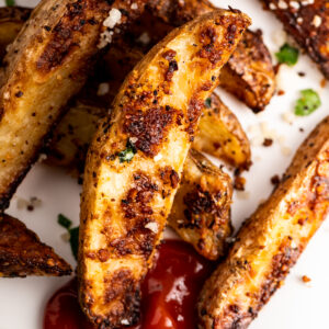 Roasted Parmesan potato wedges on a sheet pan with some ketchup.