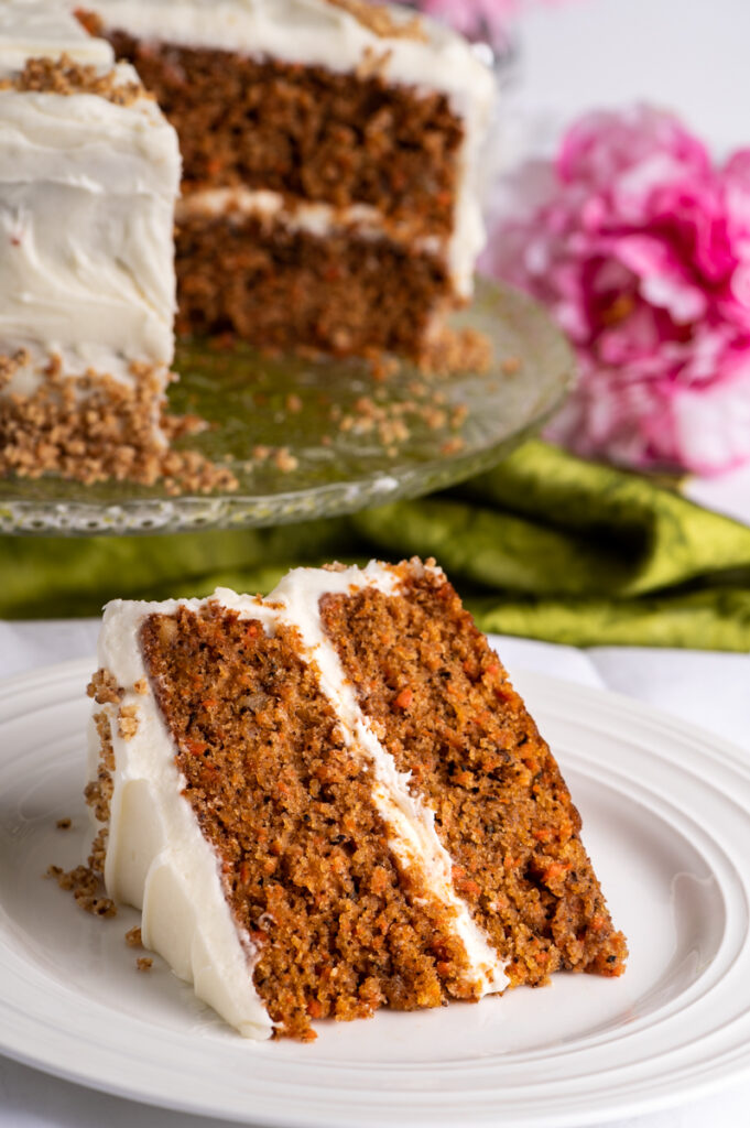 A slice of carrot cake on a plate with the cake in background.