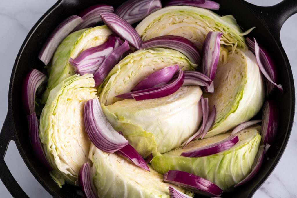 Cabbage wedges and sliced red onions in a skillet.