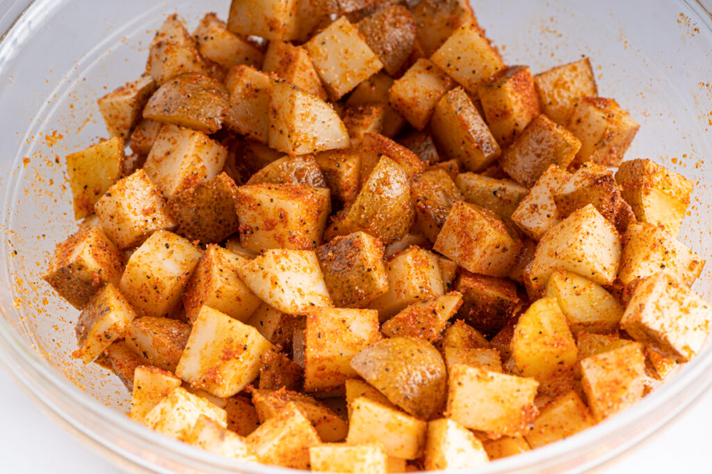 Cubes of potatoes tossed in a bowl with seasoning.
