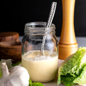 A jar of Caesar salad dressing with a bulb of garlic.