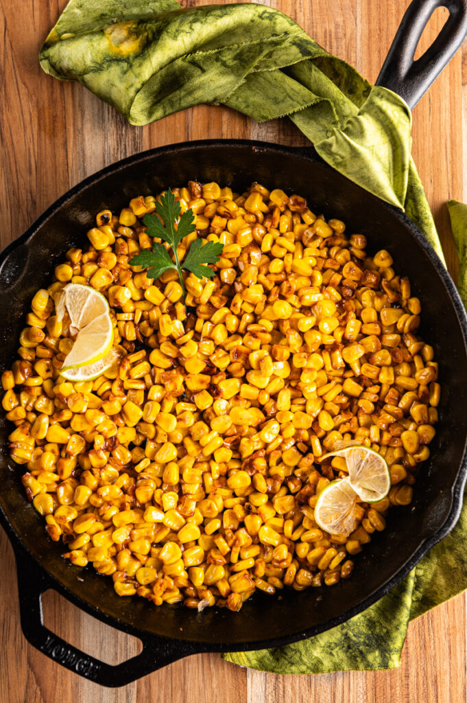A skillet of chili lime corn with sliced lime.