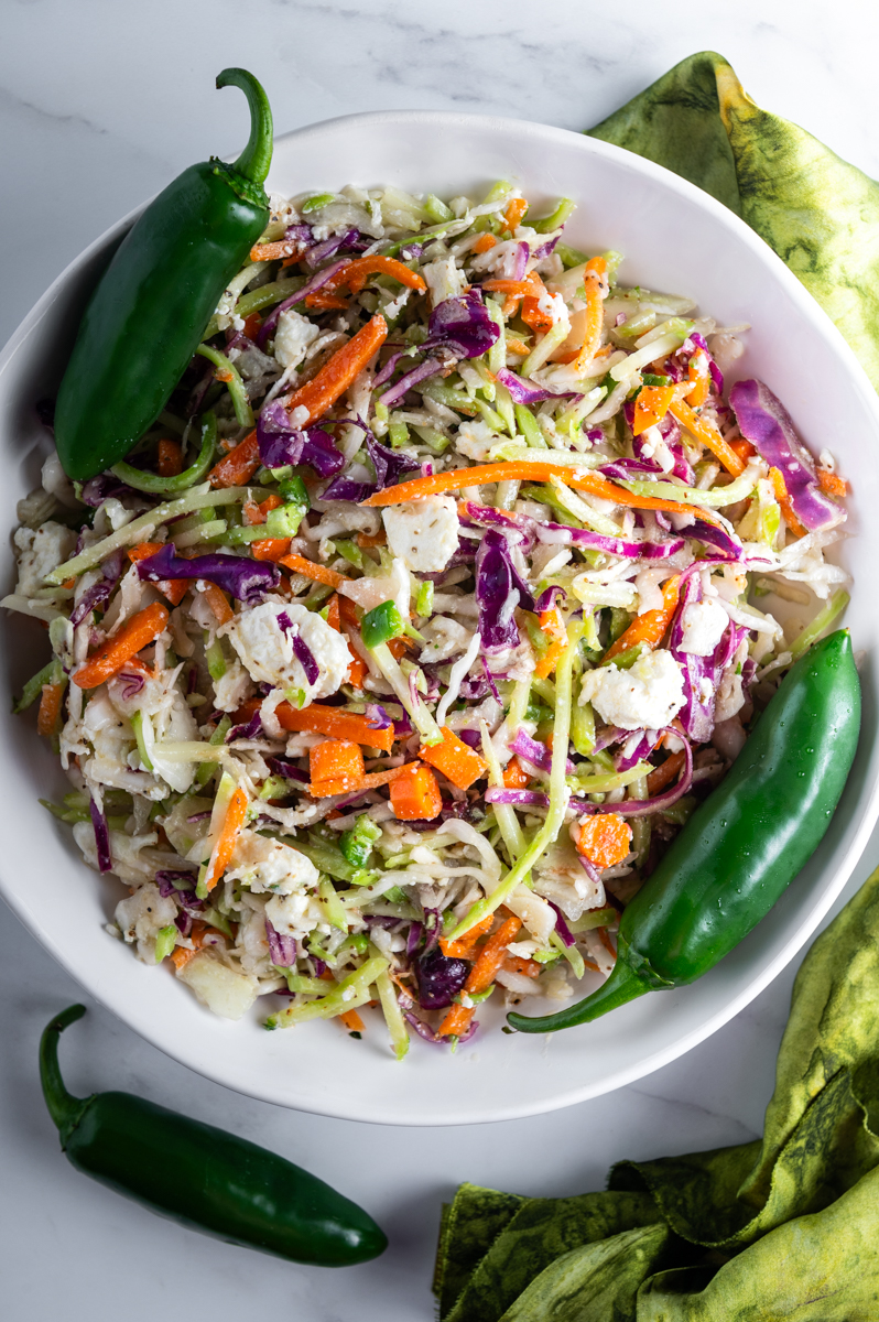 A bowl of coleslaw garnished with whole jalapeños.
