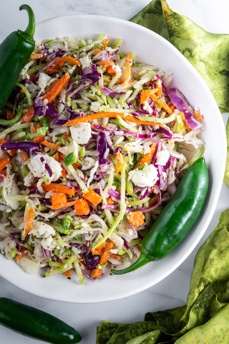 A bowl of coleslaw garnished with whole jalapeños.