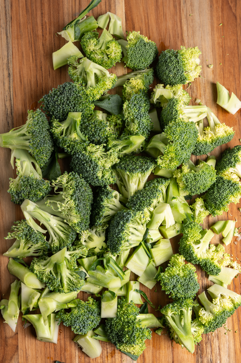 Broccoli florets and stems on a cutting board.
