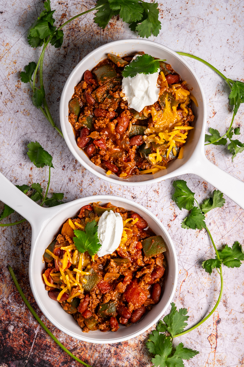 Two bowls of a simple weeknight chili garnished with sour cream and cheese.