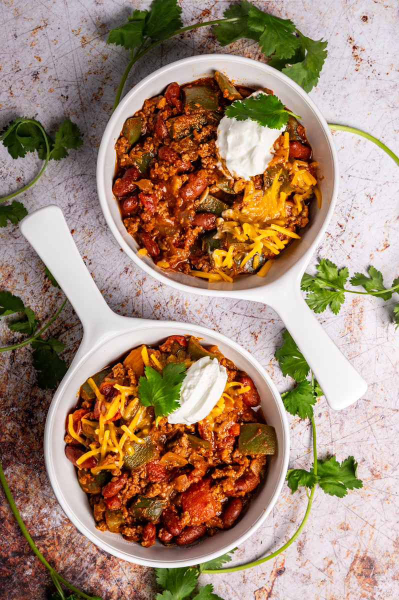 Two bowls of a simple weeknight chili garnished with sour cream and cheese.