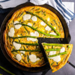 An asparagus frittata in a skillet with a slice cut.