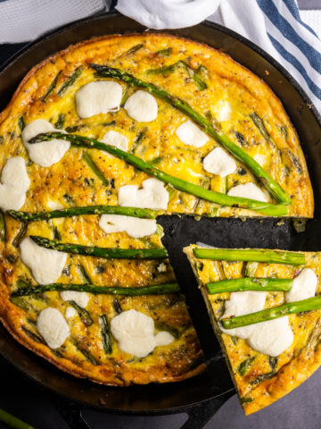 An asparagus frittata in a skillet with a slice cut.