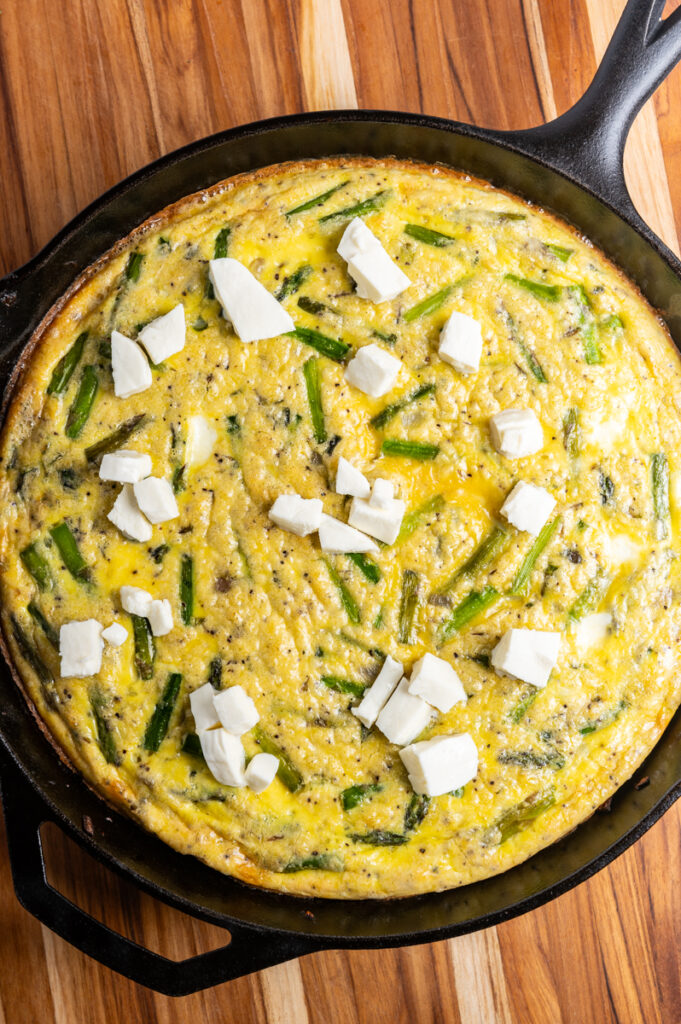 Baked asparagus frittata topped with cubed mozzarella in a cast iron skillet.