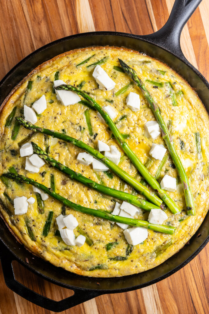 Baked asparagus frittata topped with cubed mozzarella and asparagus spears in a cast iron skillet.