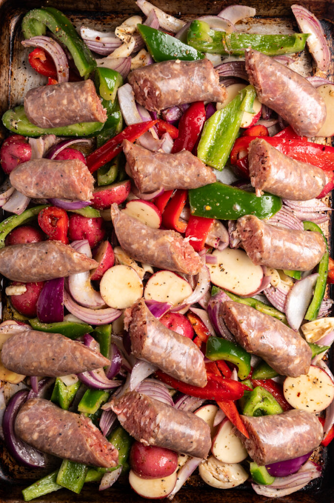 Sausages and vegetables on a baking sheet.